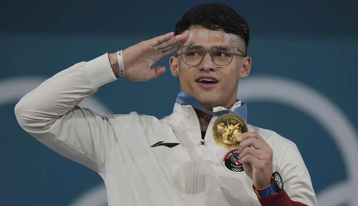 Atlet angkat besi Indonesia peraih medali emas kelas 73 kg putra cabor angkat besi Olimpiade Paris 2024, Rizki Juniansyah memberi hormat sambil menyanyikan lagu kebangsaan Indonesia Raya saat upacara penyerahan medali di Paris Expo Porte de Versailles, Paris, Kamis (8/8/2024). (AP Photo/Kin Cheung)