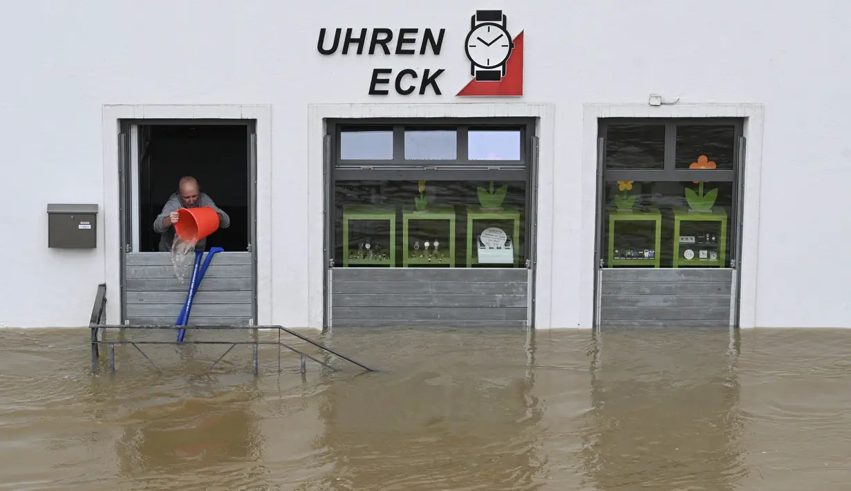 Seorang pria mencoba menumpahkan air dengan ember dari toko arlojinya di jalan dan rumah-rumah yang tergenang banjir di pusat kota Passau, Bavaria, wilayah selatan Jerman, pada 4 Juni 2024. (Michaela STACHE/AFP)