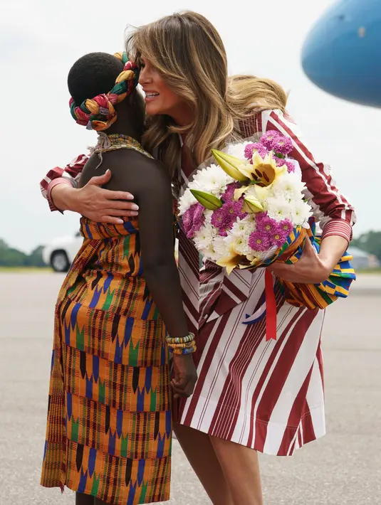 First Lady AS, Melania Trump memeluk seorang anak perempuan berpakaian tradisional Ghana setibanya di Bandara Kotoka di Accra, Selasa (2/10). Melania juga mendapatkan buket bunga yang diletakkan dalam keranjang anyaman warna-warni. (AP/Carolyn Kaster)
