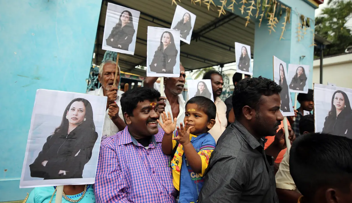 Seorang anak bertepuk tangan saat penduduk desa memegang plakat bergambar Wakil Presiden AS terpilih Kamala Harris usai berdoa khusus untuk Harris jelang pelantikannya di luar sebuah kuil Hindu di Thulasendrapuram, selatan Chennai, Tamil Nadu, India, Rabu (20/1/2021). (AP Photo/Aijaz Rahi)
