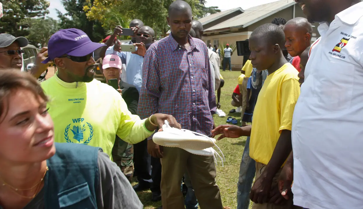 Rapper AS, Kanye West memberikan sepatu kets kepada seorang anak saat mengunjungi Kampung Anak UWESCO di Masulita, Uganda, Selasa (16/10). Kanye West membagikan ratusan pasang Yeezy Boost 350 V2s kepada anak-anak yatim piatu di sana. (AP/Stephen Wandera)