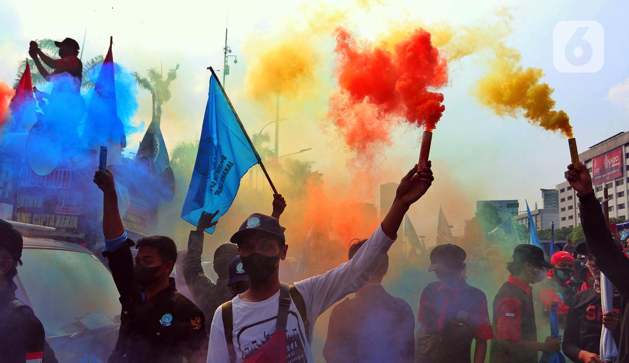 Sejumlah buruh menyalakan suar saat melakukan unjuk rasa di depan Gedung DPR, Jakarta, Rabu (10/8/2022). Dalam aksi tersebut mereka menuntut agar pemerintah menghapus Omnibus Law. (Liputan6.com/Angga Yuniar)