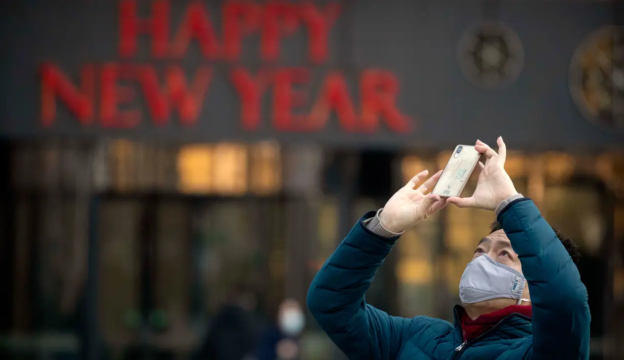 Seorang pria mengenakan masker saat mengambil foto dekorasi perayaan Imlek Tahun Tikus Logam di Beijing, 22 Januari 2020. Otoritas kesehatan China mendesak orang-orang menghindari keramaian dan pertemuan publik di Wuhan, kota yang menjadi pusat penyebaran wabah virus corona. (AP/Mark Schiefelbein)