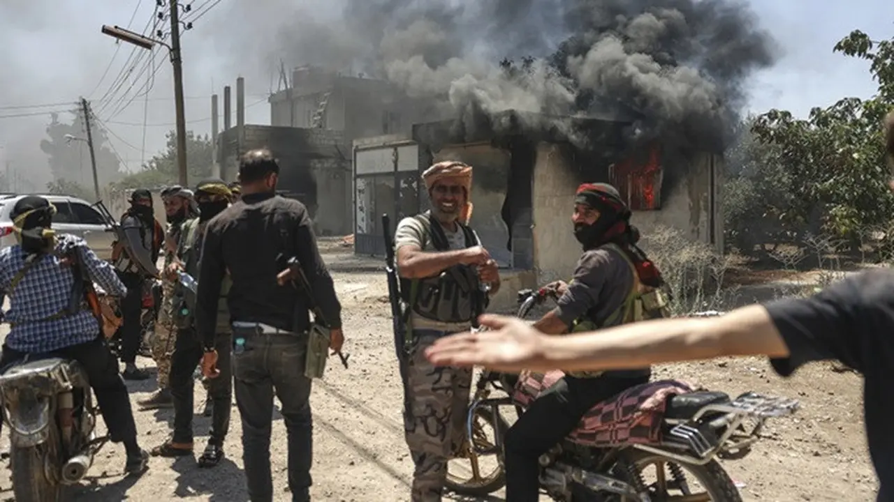 Orang-orang bersenjata Arab Badui berkumpul di depan sebuah toko yang hangus terbakar di Desa Mazraa, pinggiran Kota Sweida, di tengah bentrokan dengan milisi Druze di Suriah selatan, Jumat (18/7/2025).