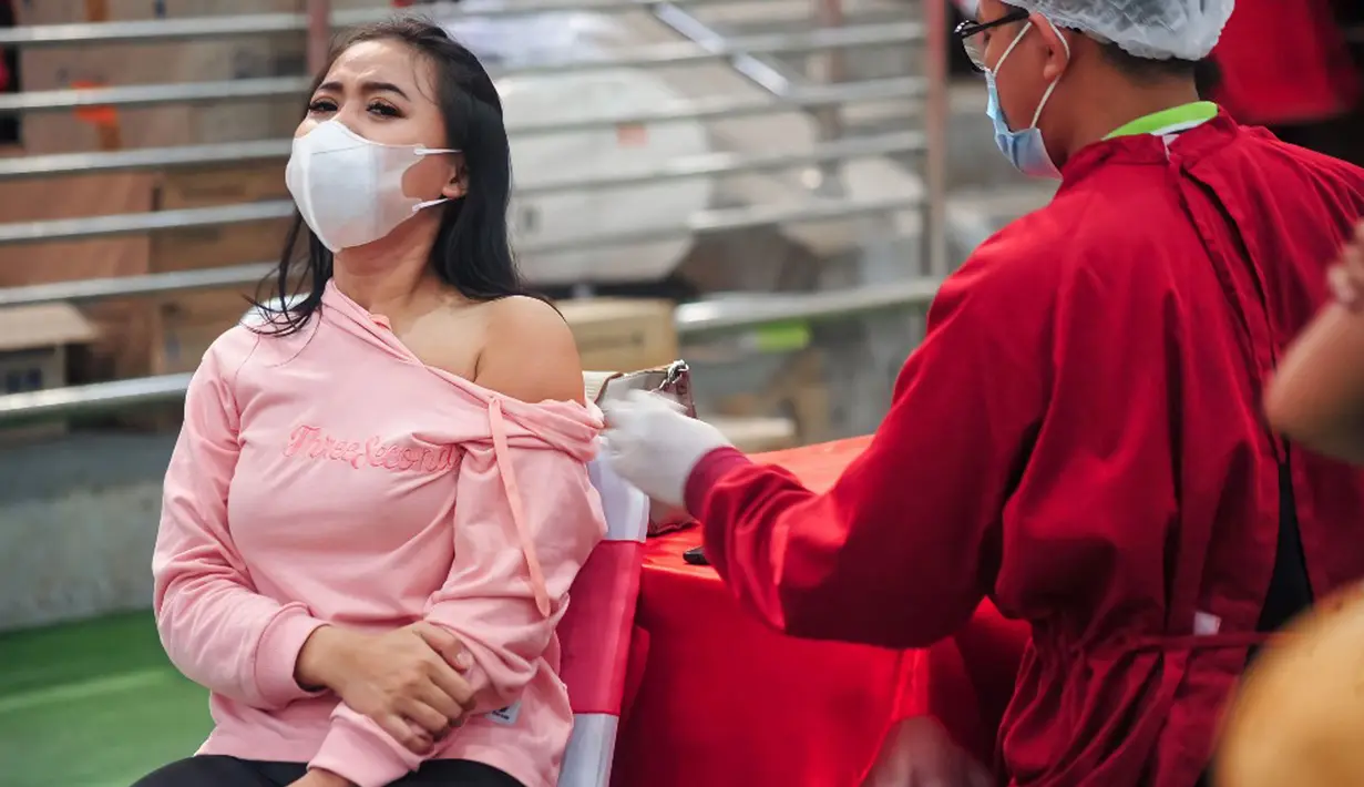 Seorang wanita menerima vaksin virus corona COVID-19 AstraZeneca di Denpasar, Bali, Sabtu (26/6/2021). Ratusan warga terlihat antusias mengikuti vaksinasi massal tersebut. (SONY TUMBELAKA/AFP)