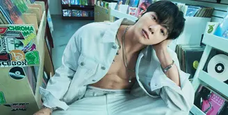 Dalam foto pertama, Jung Kook tampil berani dengan jaket denim putih yang dibiarkan terbuka tanpa inner, memperlihatkan torso atletisnya. Dipadukan dengan jeans senada berpotongan relaxed, gaya ini memancarkan maskulinitas raw yang tetap clean berkat palet monokrom. Pose santai di dalam toko piringan hitam memberi nuansa edgy sekaligus youthful.