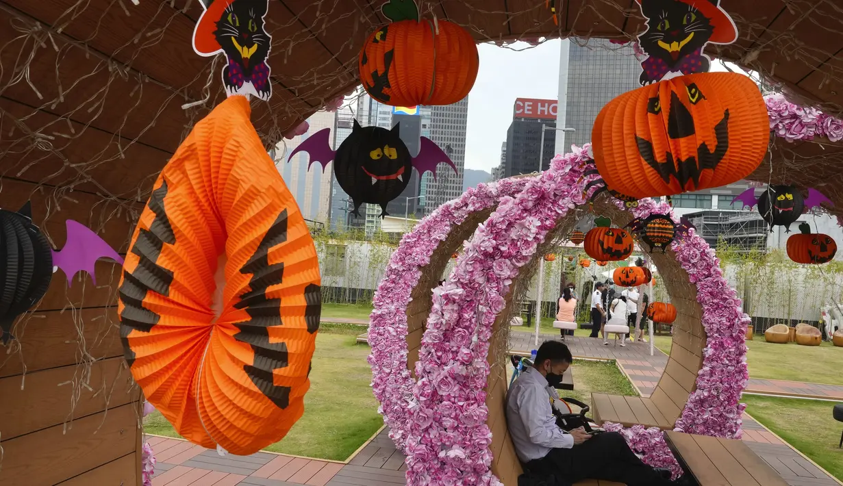 Seorang pria yang mengenakan masker untuk mencegah penyebaran virus corona, beristirahat di dekat beberapa dekorasi Halloween di sebuah taman di Hong Kong, Rabu (27/10/2021). Tahun ini, perayaan tersebut jatuh pada hari Minggu, 31 Oktober 2021. (AP Photo/Vincent Yu)