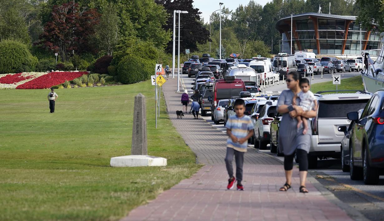 Petugas perbatasan Kanada (kiri) melihat barisan kendaraan yang menunggu untuk memasuki Kanada di perbatasan Peace Arch, Blaine, Washington, Amerika Serikat, Senin (9/8/2021). Kanada mencabut larangan terhadap warga AS yang melintasi perbatasan negaranya. (AP Photo/Elaine Thompson)