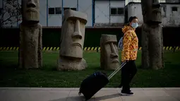 Seorang perempuan yang mengenakan masker berjalan melewati replika patung raksasa 'Moai' Pulau Paskah di Beijing pada Rabu (4/11/2020). Pulau Paskah yang berada di Negara Chile terkenal oleh patung kepala yang dipahat dari batu. (Photo by Noel Celis / AFP)
