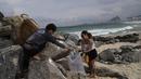 Orang-orang memungut sampah dari pantai Copacabana pada Hari Laut Sedunia di Rio de Janeiro, Brasil, Rabu (8/9/2022). Organisasi Route Brasil menyerukan agar orang-orang berkumpul untuk acara yang diberi nama "Pelukan Itu," dan untuk memungut sampah di pantai, untuk menarik perhatian pada pencemaran laut. (AP Photo/Silvia Izquierdo)
