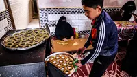 Anggota keluarga Palestina menyiapkan kue-kue tradisional untuk dijual sebagai persiapan liburan Idul Fitri mendatang, di kota Rafah, Jalur Gaza, Selasa (4/5/2021). Pembuatan kue tradisional untuk Hari Raya Idul Fitri atau Lebaran yang akan datang menandai akhir bulan Ramadhan. (KATA KHATIB/AFP)