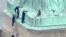 Petugas kepolisian membujuk seorang wanita yang memanjat Patung Liberty di New York, Rabu (4/7). Aksi yang digelar bersamaan dengan Hari Kemerdekaan AS tersebut dilakukan sebagai bentuk protes penanganan imigran oleh pemerintah AS. (AFP/PIX11 News/HO)