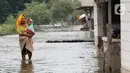 Seorang ibu menggendong anaknya sambil menerobos banjir rob yang menggenangi rumah dan tambak warga di Desa Pantai Mekar, Muaragembong, Bekasi, Senin (6/12/2021). Banjir rob telah menggenangi wilayah tersebut selama empat hari akibat kenaikan permukaan air laut. (Liputan6.com/Herman Zakharia)