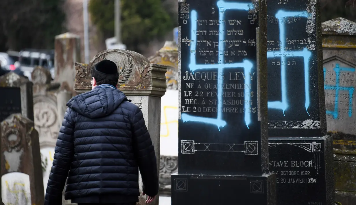 Seorang pria berjalan melewati makam Yahudi yang dicoret simbol Nazi di pemakaman Yahudi, Quatzenheim, Prancis, Selasa (19/2). Aksi vandalisme ini dilakukan terhadap sekitar 80 makam. (Frederick FLORIN/AFP)