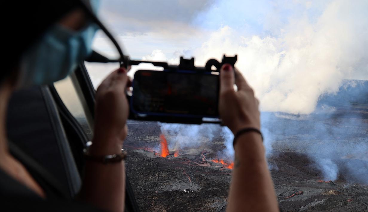 Seorang perempuan mengambil gambar gunung berapi Piton de la Fournaise yang meletus di pulau Reunion, Samudra Hindia Prancis. Gunung yang memiliki ketinggian 2632 meter ini meletus untuk kedua kalinya dalam setahun pada 22 Desember pukul 3:30 (12:30 di Paris).  (Richard BOUHET/AFP)