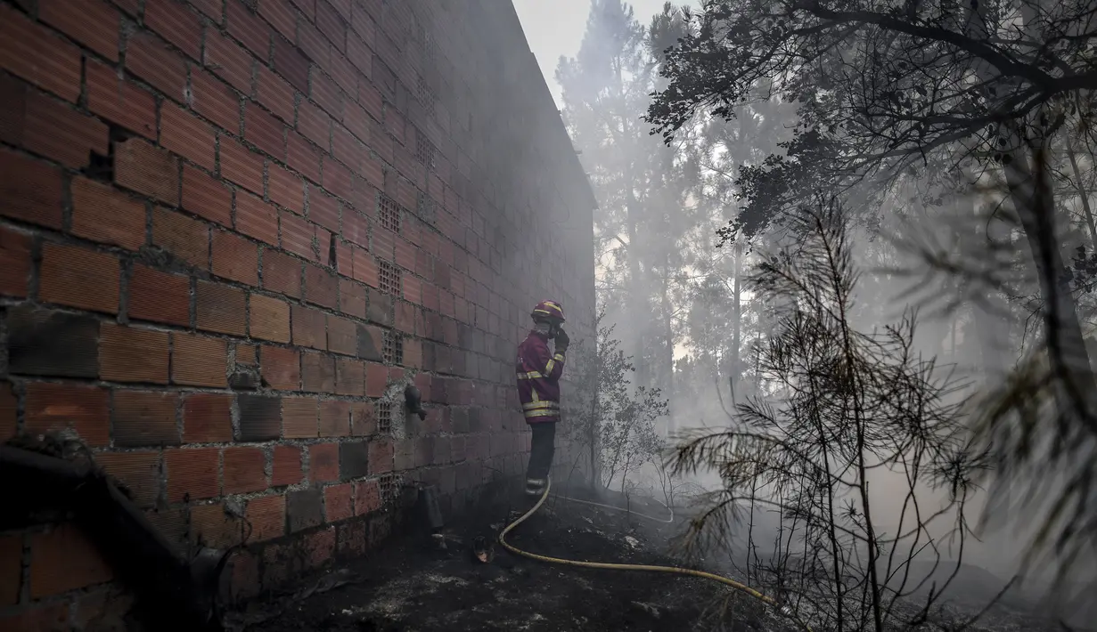 Seorang petugas pemadam kebakaran berdiri di sebelah sebuah rumah setelah kebakaran hebat di Sarnadas, Macao, di Portugal tengah (21/7/2019). Puluhan orang tewas akibat  kebakaran hutan tersebut. (AFP Photo/Patricia De Melo Moreira)