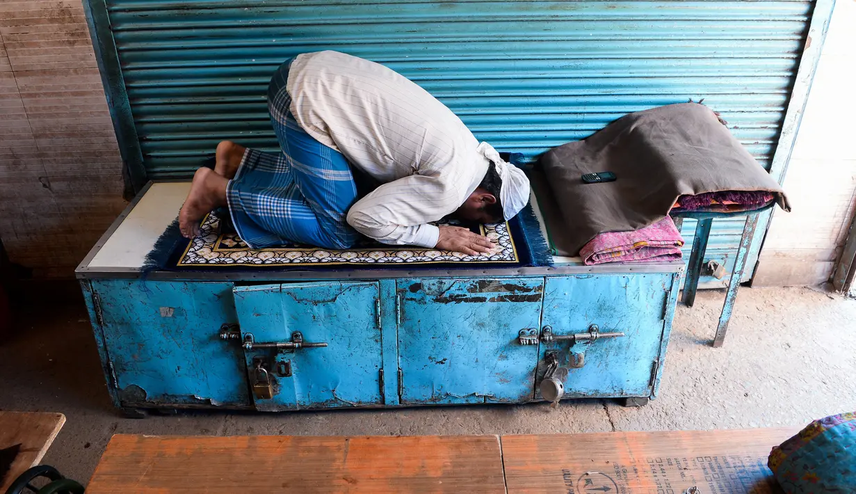 Umat Muslim melaksanakan salat di depan toko-toko yang tutup di sebuah pasar selama bulan Ramadan saat penerapan lockdown di New Delhi, Senin (4/5/2020). Di emperan toko-toko yang tutup, umat muslim salat berjemaah dengan menjaga jarak dan lainnya membaca kitab suci Alquran. (Sajjad HUSSAIN/AFP)