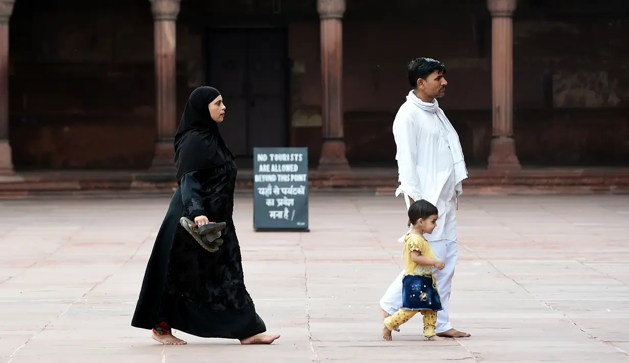 Seorang pria bersama istri dan anaknya berjalan di masjid Jama  di kawasan lama New Delhi, India (30/7/2019). Masjid Jama sendiri terletak di sisi jalan raya yang sangat ramai di Delhi Tua, yaitu Jalan Chadni Chowk. (AFP Photo/Money Sharma)