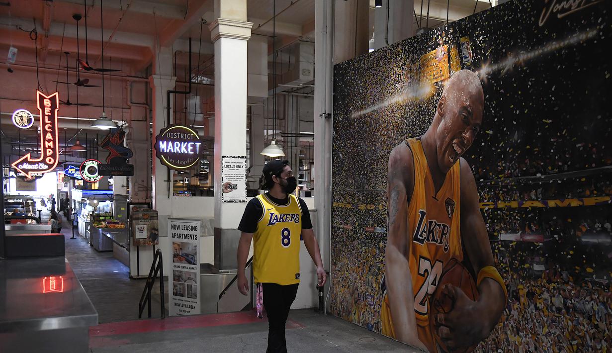 Seorang fans melintas di depan lukisan mural bintang LA Lakers, Kobe Bryant di Grand Central Market, Los Angeles, California, Selasa (26/1/2021). Lukisan dibuat untuk mengenang 1 tahun tragedi kecelakaan helikopter yang menewaskan Kobe Bryant dan putrinya, Gianna. (Getty Images via AFP/Sarah Stier)