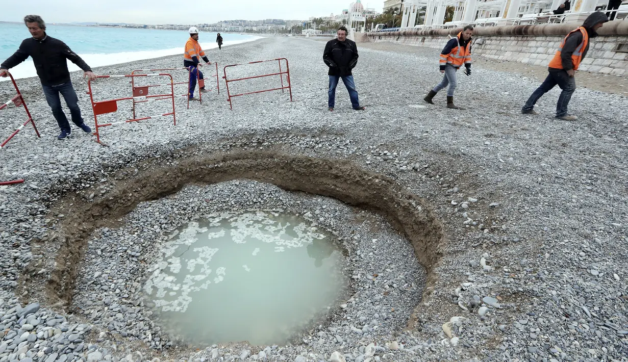 Petugas memasang paga besi mengelilingi kawah misterius berisi air payau yang muncul di Pantai Lido, Nice, Prancis, Kamis (1/2). Lubang selebar 5 meter dan sedalam 2 meter itu membuat banyak warga sekitar kebingungan. (VALERY HACHE/AFP)