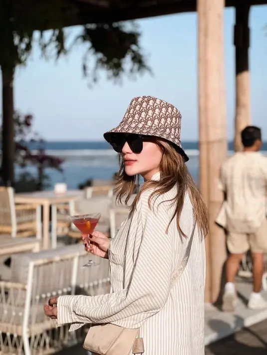 Foto Hilda Vitria saat berlibur di Bali pun tak kalah mencuri perhatian. Dia mengenakan kemeja longgar berwarna krem dan topi berwarna senada. (Foto: Instagram/ hvkhildavitriakhan)