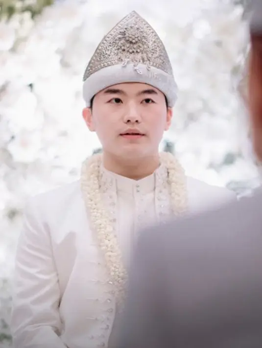 Beskap putih yang dipadu dengan celana panjang serasi dan kain wastra sebagai penutup celana dan hiasan kepalanya. [Foto: Instagram/bootesphotography]