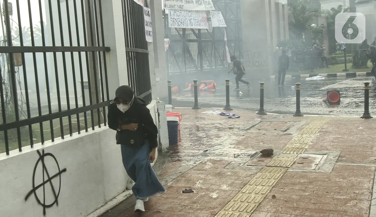 Seseorang berlari menghindari tembakan gas air mata oleh aparat keamanan di depan Gedung DPR, Jakarta, Senin (11/4/2022). Mahasiswa yang tergabung dalam aliansi BEM SI menggelar unjuk rasa besar-besaran di depan Gedung DPR/MPR RI, Senin ini. (Liputan6.com/Angga Yuniar)