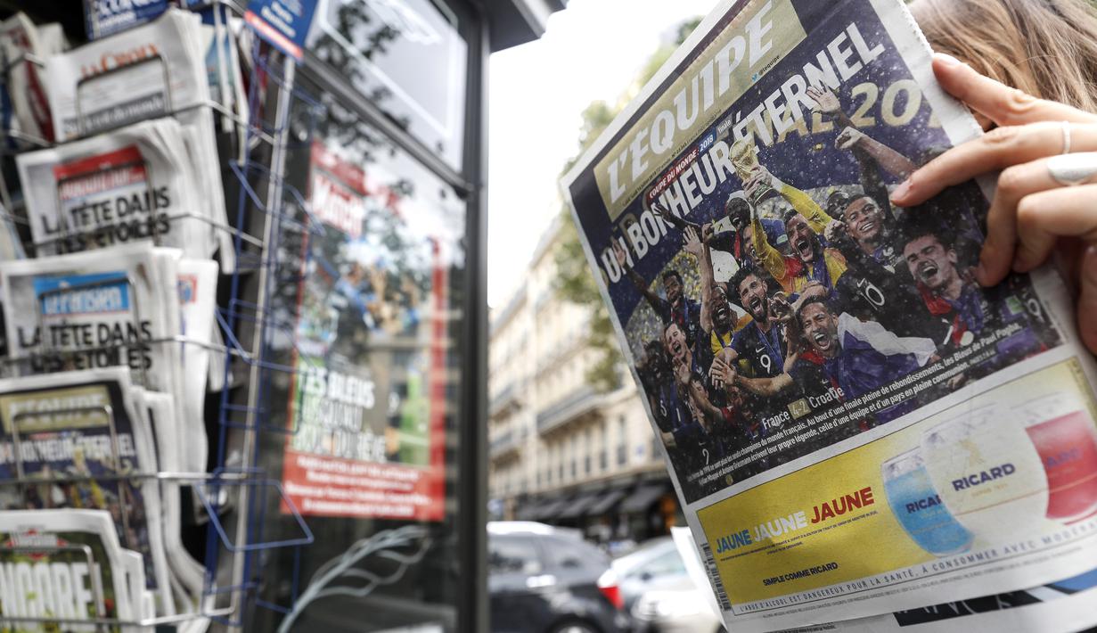 Seorang wanita sedang membaca koran dengan halaman depan berjudul "Eternal Happiness"  di Paris (16/7/2018). Prancis berpesta merayakan keberhasilan Les Bleus meraih trofi Piala Dunia 2018. (AP/Jean-Francois Badias)