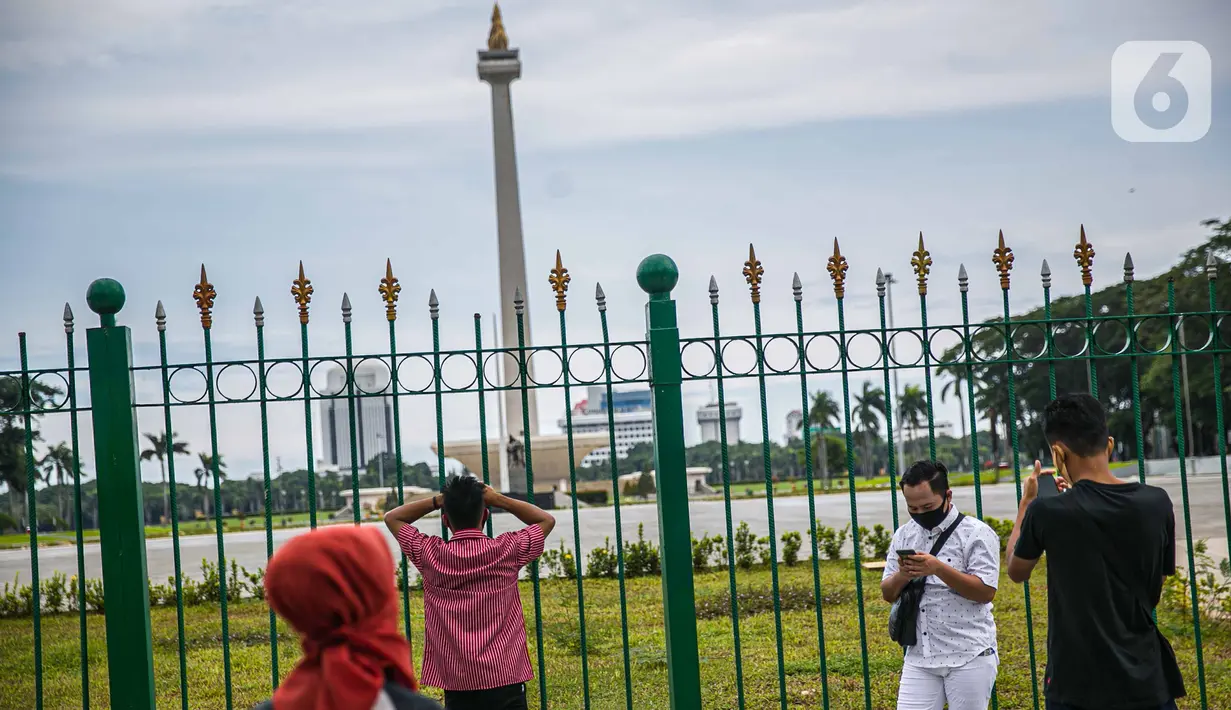 Warga berfoto di belakang Monumen Nasional atau Monas di Jakarta, Jumat (1/1/2021). Kebijakan ini bertujuan untuk mengurangi kerumunan massa di sejumlah objek wisata saat libur Tahun Baru di Jakarta. (Liputan6.com/Faizal Fanani)
