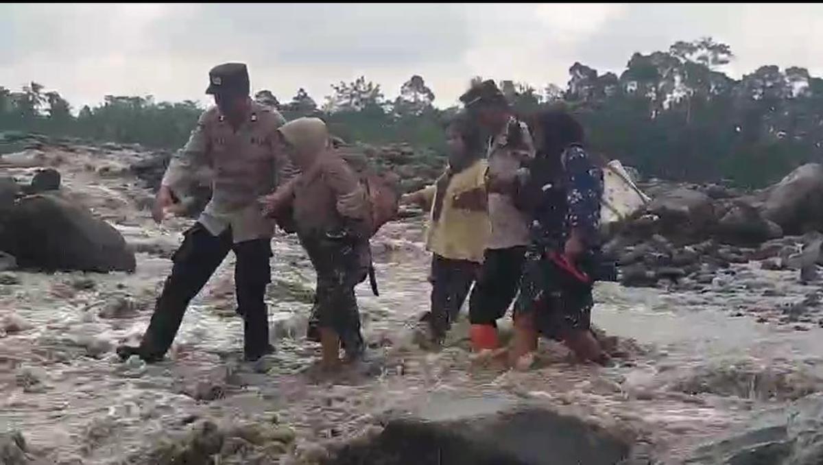 Anggota Polsek Candipuro membantu pelajar menyeberangi sungai aliran lahar di Desa Jugosari untuk pergi ke sekolah