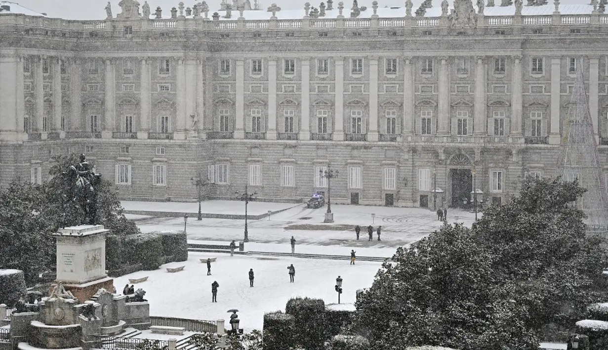 Orang-orang berjalan melewati salju di luar Istana Kerajaan, Madrid, Spanyol, Jumat (8/1/2021). Salju tebal menutupi hingga setengah dari Spanyol dan menyebabkan penurunan suhu yang besar. (GABRIEL BOUYS/AFP)