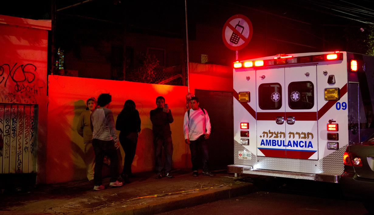 Warga setempat berdiri diseberang garasi parkir bawah tanah yang runtuh di sebuah kompleks di Mexico City (10/4). (AP Photo/Rebecca Blackwell)