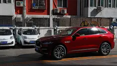 Sebuah mobil SUV warna merah melintas di depan mobil listrik model lama yang diparkir di stasiun pengisian listrik di rumah hunian Beijing (14/04/2017). Penjualan mobil kesulitan karena minimnya stasiun pengisian listrik. (AP Photo / Andy Wong)