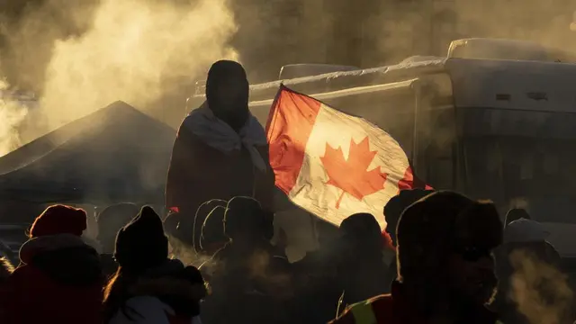 Seorang pengunjuk rasa berdiri di barikade ketika truk terus memblokir pusat kota sebagai protes atas pembatasan COVID-19, di Ottawa, Ontario, Sabtu, 5 Februari 2022. (Adrian Wyld/The Canadian Press via AP)