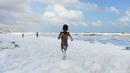 Seorang anak berlari di atas limbah busa yang disebabkan polutan saat bercampur dengan ombak di pantai di Chennai (29/11/2019). Limbah mencapai laut melalui sungai, memicu busa beracun di pantai tersebut. (AFP/Arun Sankar)