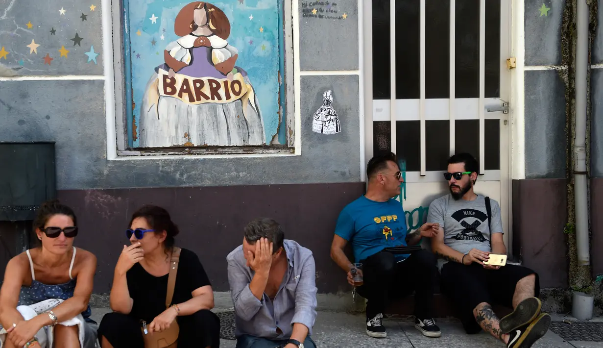 Warga duduk di samping mural yang terinspirasi oleh karya Velazquez "Las Meninas" selama festival seni jalanan tahunan di Ferrol, Spanyol, Minggu (2/9). (MIGUEL RIOPA/AFP)
