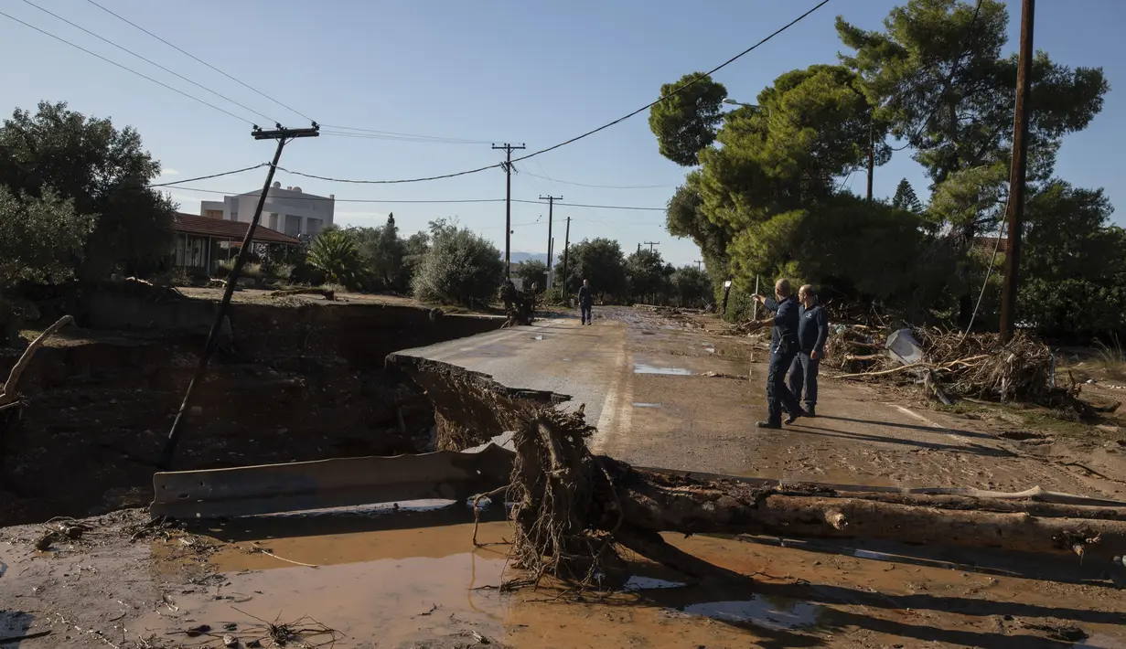 Warga memeriksa jalan yang rusak setelah badai di desa Kineta, Athena (25/11/2019). Ratusan rumah terendam banjir setelah badai semalam menerjang daerah barat Athena. (AP Photo/Petros Giannakouris)