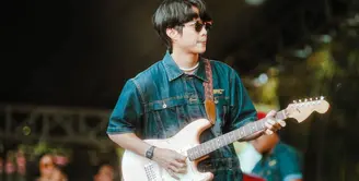 Dikta dalam balutan benetton jumpsuit denim lengan pendek berkerah. Ia tampil di atas panggung, sedang memainkan gitar dengan sunglasses. Foto: Instagram.