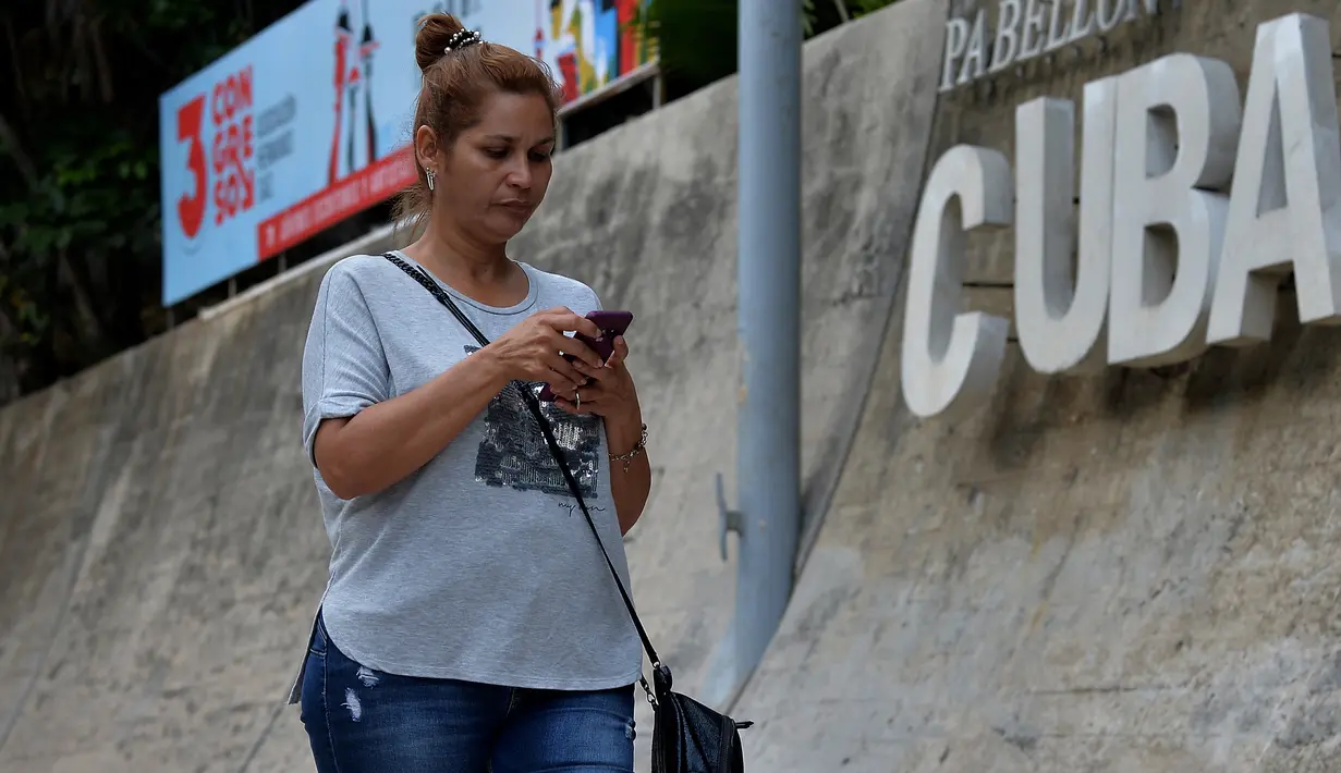 Seorang wanita menggunakan ponselnya untuk terhubung ke internet melalui WiFi di Havana, Rabu (5/12).Hampir setengah dari 11,2 juta penduduk Kuba memiliki ponsel, namun tidak semua akan mampu membeli paket internet ponsel. (YAMIL LAGE/AFP)