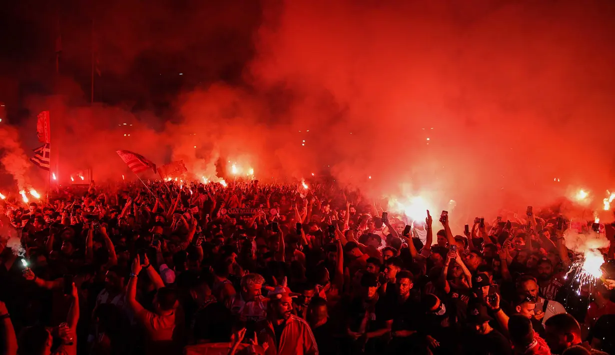 Di luar lapangan, suporter Olympiakos menyalakan suar saat merayakan gelar juara Europa Conference League. (Aris Oikonomou/AFP)