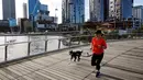 Seorang wanita berlari dengan anjingnya melalui Elizabeth Quay di Perth (29/6/2021). Kota ini mengikuti Sydney dan Darwin melakukan lockdown untuk menahan wabah baru varian Delta yang sangat menular. (AFP/Trevor Collens)