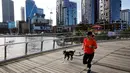 Seorang wanita berlari dengan anjingnya melalui Elizabeth Quay di Perth (29/6/2021). Kota ini mengikuti Sydney dan Darwin melakukan lockdown untuk menahan wabah baru varian Delta yang sangat menular. (AFP/Trevor Collens)