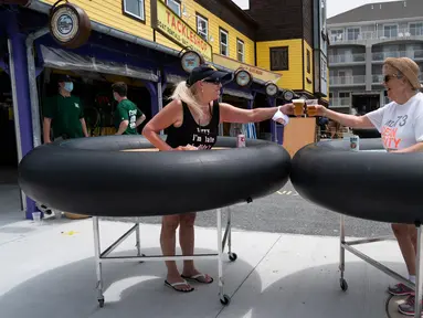 Para tamu mencoba meja portabel yang bentuknya menyerupai ban pelampung untuk menjaga jarak pelanggan di Fish Tales Bar & Grill di Ocean City, Maryland, Jumat (29/5/2020). Pengunjung akan berdiri di bagian tengah meja bundar itu yang dilengkapi roda untuk memudahkan pergerakan. (Alex Edelman/AFP)