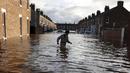 Seorang pria melintasi banjir yang merendam jalan pemukiman di Carlisle, Inggris, Minggu (6/12). Puluhan ribu rumah tidak punya listrik karena Badai Desmond yang menyebabkan banjir di Inggris utara dan sebagian Skotlandia. (REUTERS/Phil Noble)