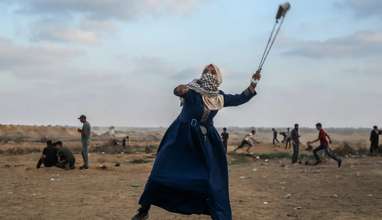 Wanita Palestina memakai ketapel untuk melemparkan batu ke arah pasukan Israel saat bentrok di Khan Yunis, Jalur Gaza, Jumat (13/9/2019). Unjuk rasa ini digelar setiap Jumat untuk menuntut kepulangan ke Tanah Palestina. (SAID KHATIB/AFP)