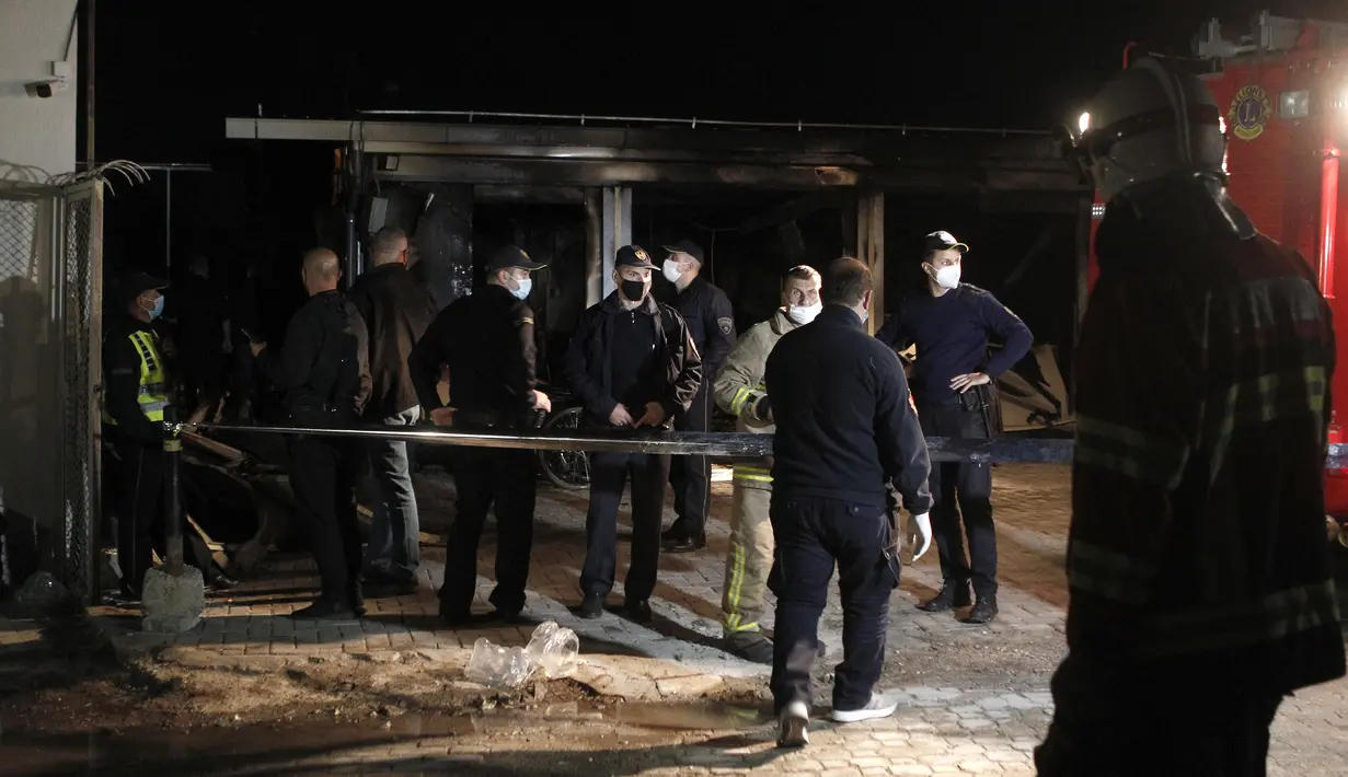 Petugas pemadam kebakaran dan polisi berdiri di dekat rumah sakit darurat yang terbakar di kota Tetovo, Makedonia Utara, Kamis (9/9/2021). Belum diketahui penyebab kebakaran, penyelidikan masih berlangsung. (AP Photo/Boris Grdanoski)