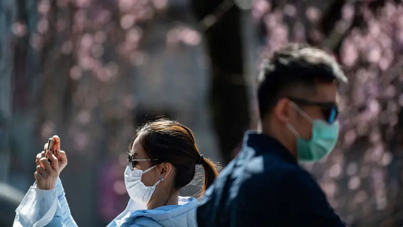Pengunjung mengenakan masker wajah di tengah kekhawatiran akan penyebaran Virus Corona COVID-19 di hadapan pohon ceri di Taman Ueno Tokyo Jepang pada 12 Maret 2020. (Philip FONG / AFP)