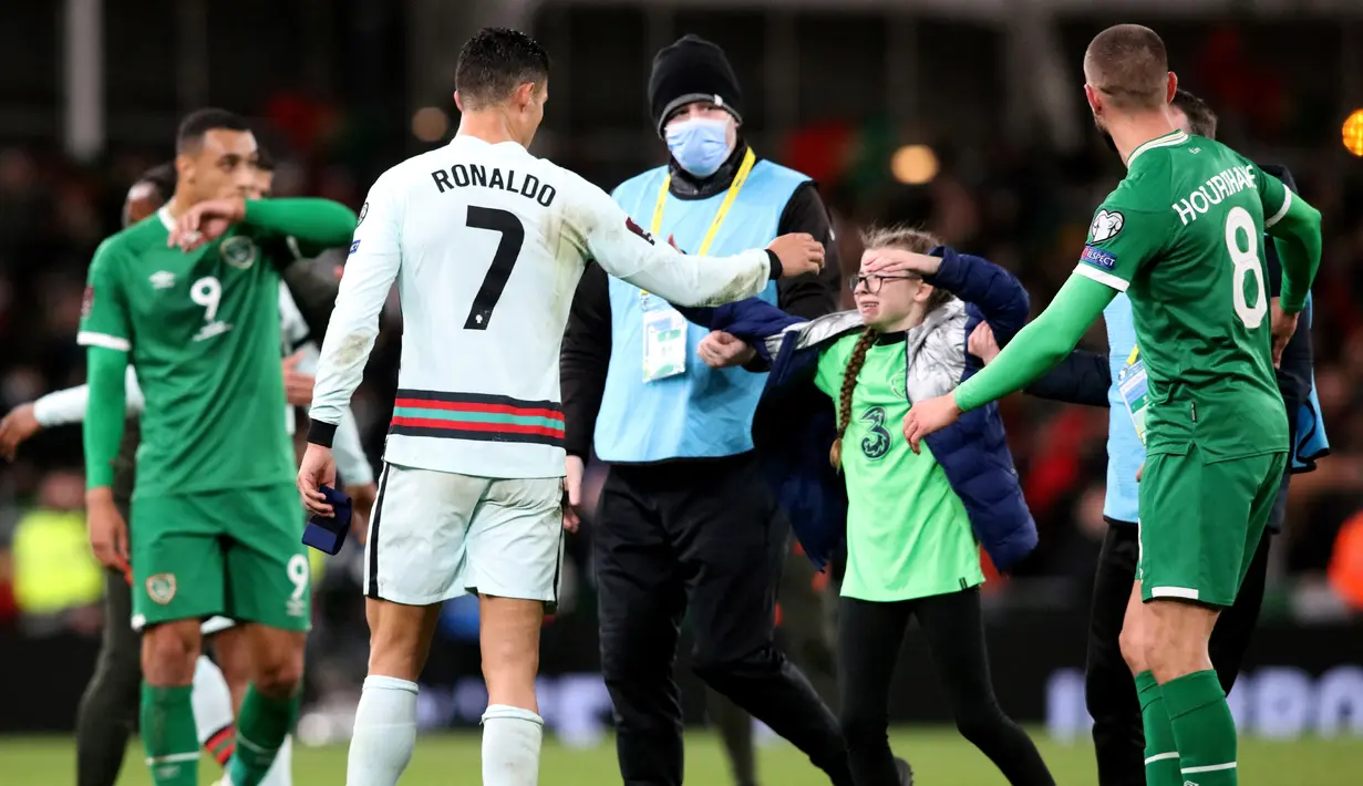 Seorang fans cilik berusaha memeluk striker Portugal Cristiano Ronaldo setelah berlari ke lapangan pada akhir laga Grup A Kualifikasi Piala Dunia 2022 Zona Eropa melawan Irlandia di Stadion Aviva, Jumat (12/11/2021) dinihari WIB. Fans itu nekat menerobos petugas keamanan stadion. (Paul Faith / AFP)
