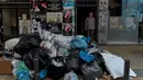 Seorang pria berdiri di belakang tumpukan sampah di pusat kota Athena, Kamis (22/6). Tumpukan sampah tampak menggunung di beberapa kota di Yunani sejak awal pekan ini setelah ribuan petugas pengumpul sampah melakukan mogok kerja. (ELEFTHERIOS ELIS/AFP)