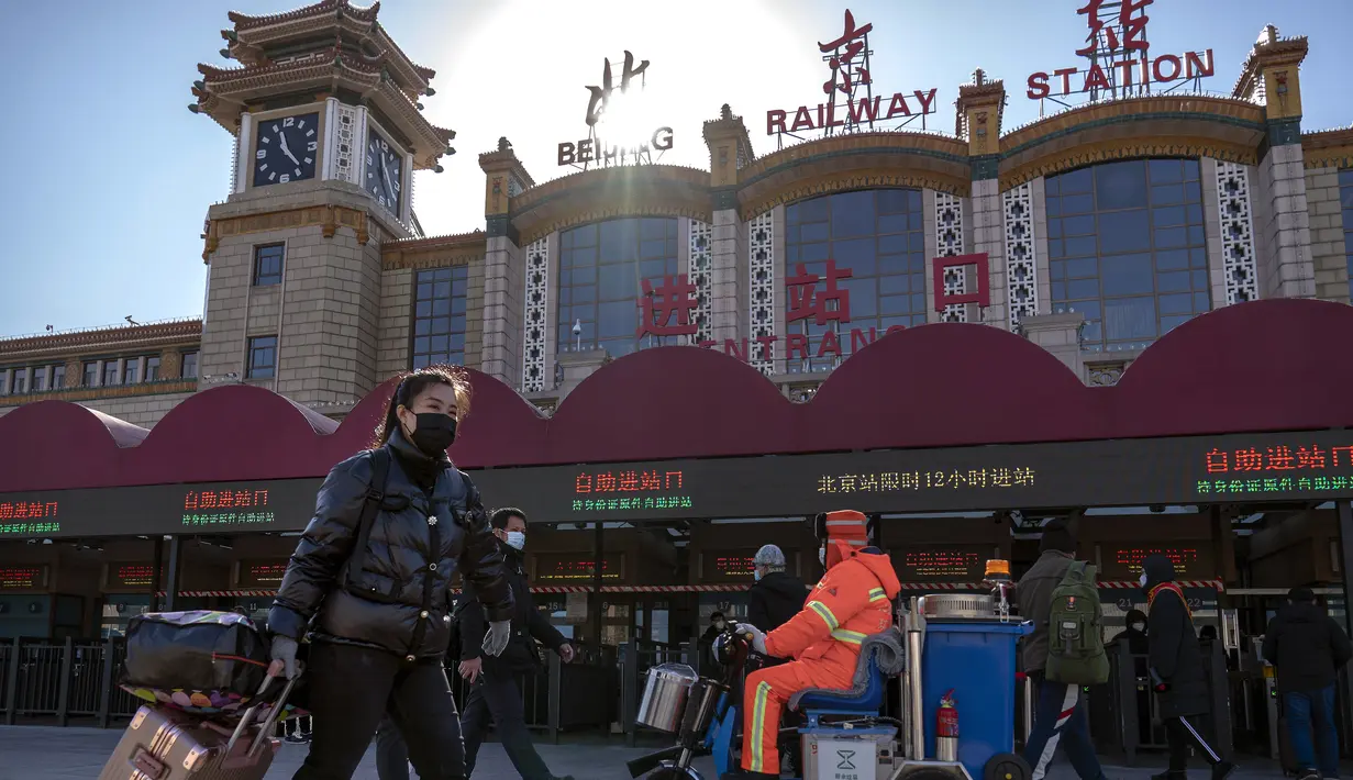 Wisatawan yang mengenakan masker untuk melindungi dari penyebaran virus corona berjalan dengan membawa barang bawaan mereka di Stasiun Kereta Api Beijing di Beijing, Kamis (28/1/2021).  Upaya untuk mencegah warga Tiongkok bepergian untuk Tahun Baru Imlek tampaknya berhasil. (AP Photo/Mark Schiefelb